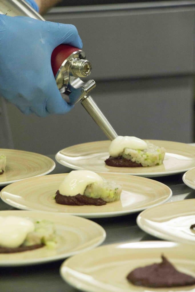 Koch im 'August und Maria' tr&auml;gt Sauce Hollandaise auf Bachforelle auf.
